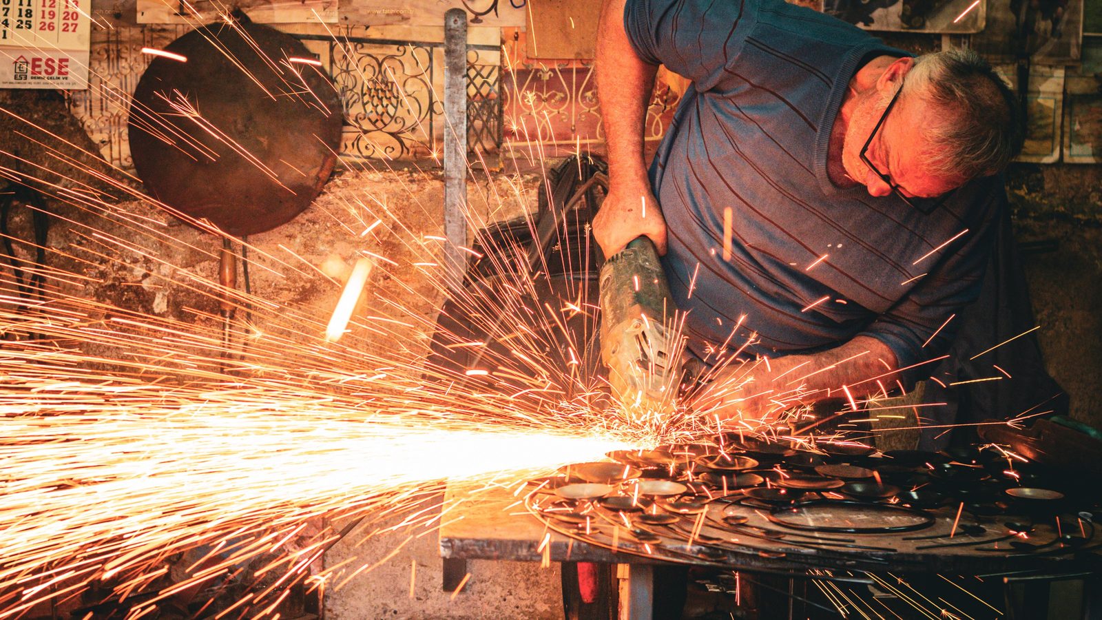Un artisan ferronnier meule une pièce dans son atelier, dans une gerbe d'étincelles